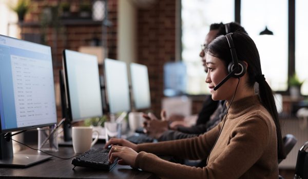 Paralyzed asian employee working at call center reception in disability friendly office. Female operator wheelchair user with impairment giving assistance on customer service helpline.