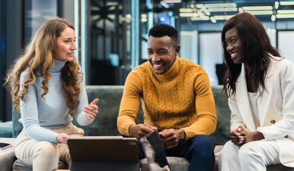 Multiracial group of people in an office discussing business while sitting on a sofa, tablet on the table